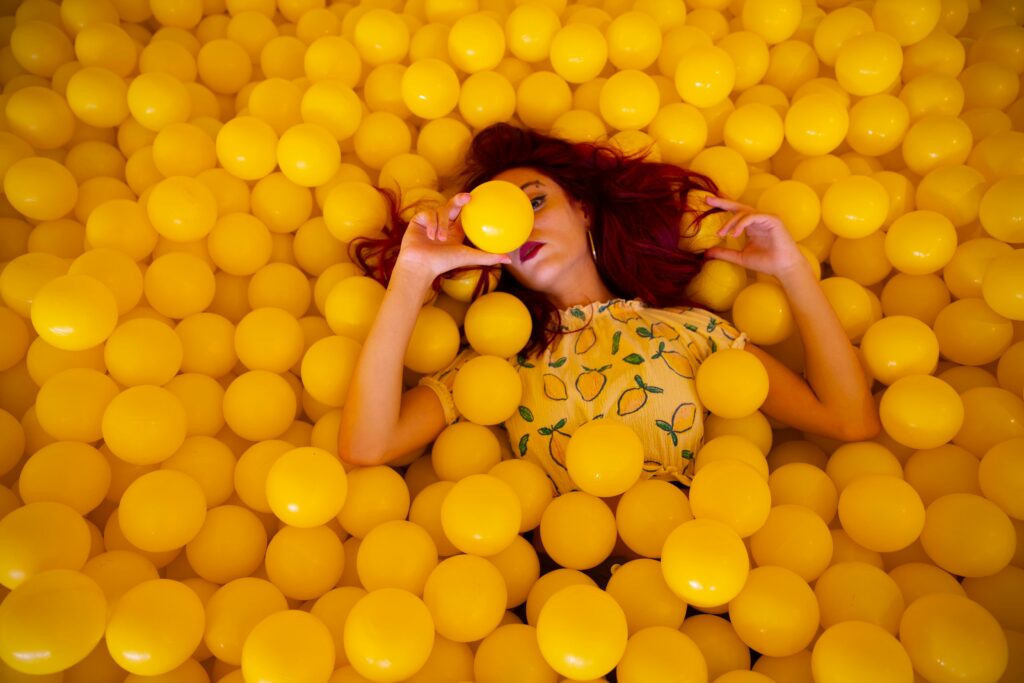 How to stay anonymous at hookup sites? Safety tips for hookup & dating sites 3 Woman with red hair in a yellow ball pit, creating a colorful and playful portrait.